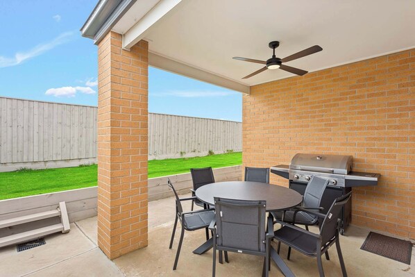 An outdoor patio with a round table and chairs, a grill, and a ceiling fan.