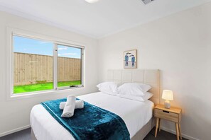 Un dormitorio con cama, ventana, mesita de noche y un cuadro colgado en la pared.