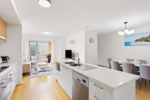 A modern kitchen with a dishwasher, a dining area with a table and chairs, and a living area with a sofa and a TV. - Family-Friendly Coastal Retreat with Modern Amenities (Cowes)