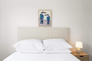 A bed with white bedding, a headboard, and a bedside table with a lamp.