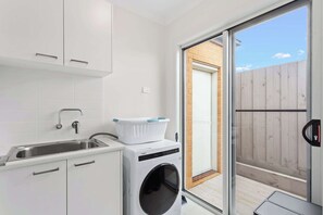 A compact laundry room with a washing machine, a sink, and a drying rack.