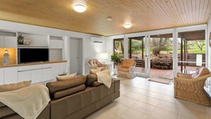 A modern living room with a sofa, chairs, a TV, and a glass door leading to an outdoor area. - Private Access to Beach, Oceanview with Home Gym (Silverleaves)