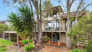 A two-story building with a patio area, surrounded by trees and plants. - Private Access to Beach, Oceanview with Home Gym (Silverleaves)