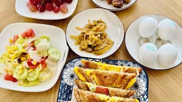 Une table où l’on trouve différents plats, notamment une salade, des œufs au plat et une assiette de viande.