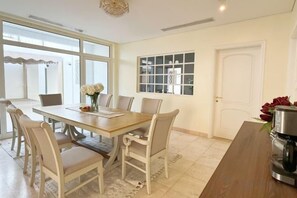 Un comedor con una mesa y sillas de madera, una ventana con cortinas blancas y una puerta con panel de vidrio.