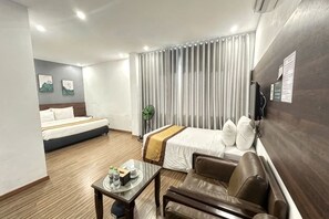 Una habitación de hotel con cama, escritorio con una bandeja de objetos, sofá y un ventanal con cortinas.