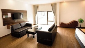 Un salon moderne comprenant un canapé, une table basse, un téléviseur à écran plat fixé au mur, une grande fenêtre avec des rideaux et une tête de lit incurvée originale.