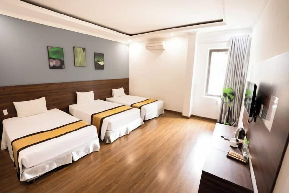Une chambre d’hôtel avec trois lits, un plancher en bois, un bureau avec un miroir et des œuvres d’art accrochées au mur.