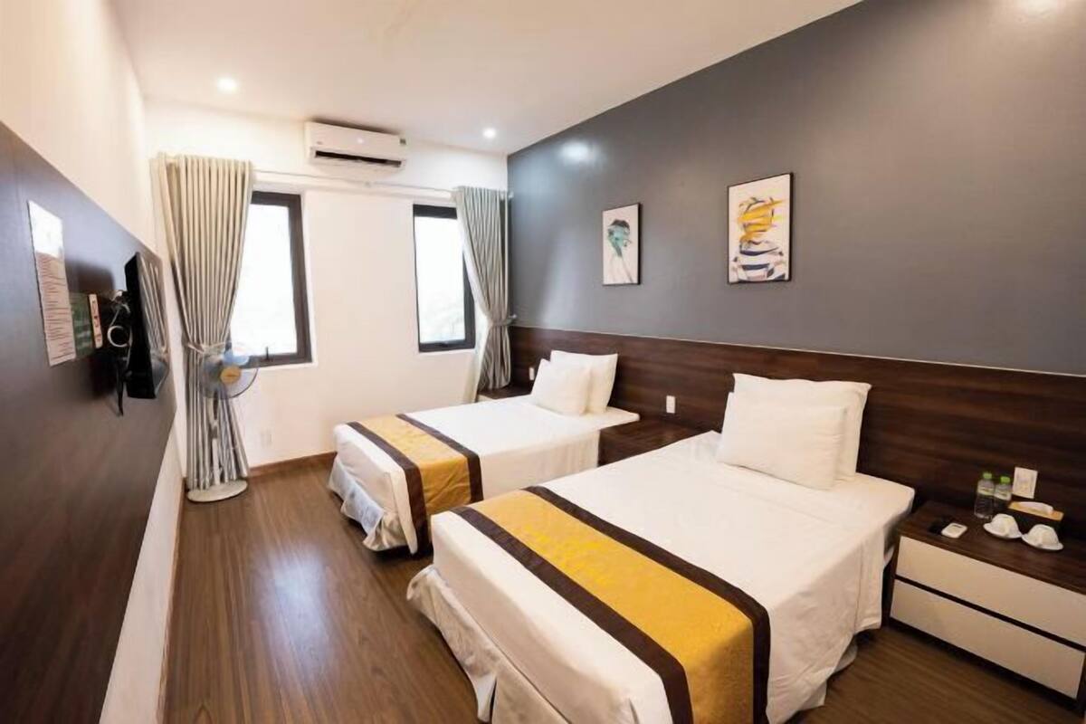 Une chambre d’hôtel avec deux lits, un plancher en bois, une table de chevet avec des articles de toilette et une fenêtre avec des rideaux.