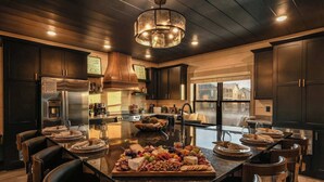 Une cuisine moderne avec des meubles en bois foncé, un réfrigérateur en acier inoxydable et un grand îlot central agrémenté d’une planche à découper pour la charcuterie.