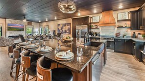 Une cuisine moderne dotée d’un grand îlot central, de meubles en bois foncé, d’appareils électroménagers en acier inoxydable et d’un luminaire suspendu.