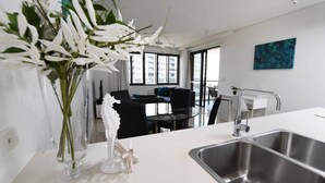 Eine moderne Küche mit Spüle aus Edelstahl, einer Vase mit weißen Blumen und einem Essbereich im Hintergrund.