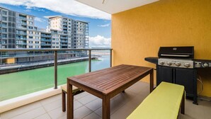 Ein Balkon mit Tisch und Grill, mit Blick auf einen Fluss und Gebäude.