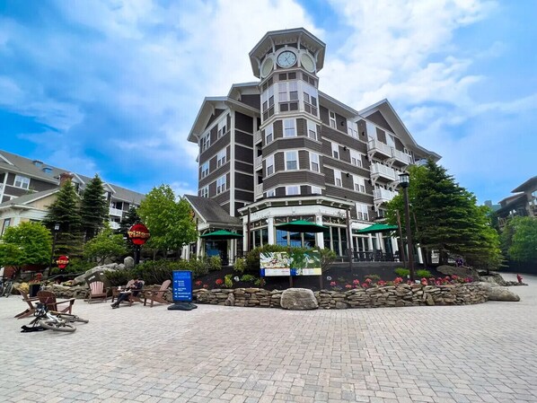 A multi-story hotel with a distinctive corner tower, outdoor seating area, and a landscaped garden.