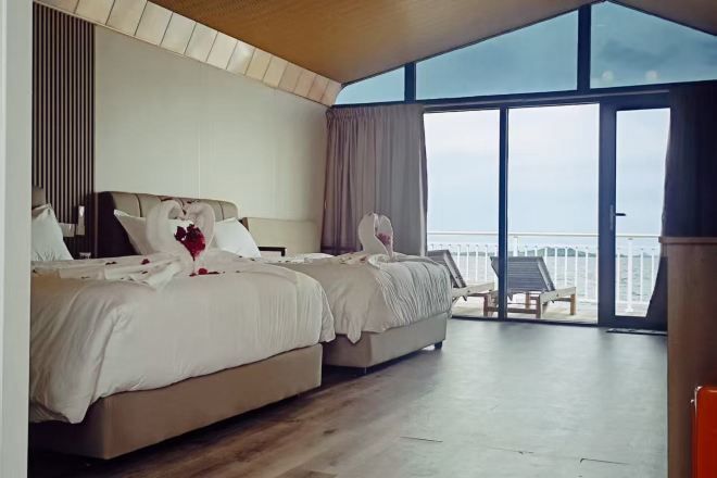 Habitación de hotel con dos camas, un ventanal grande y un balcón con una silla.