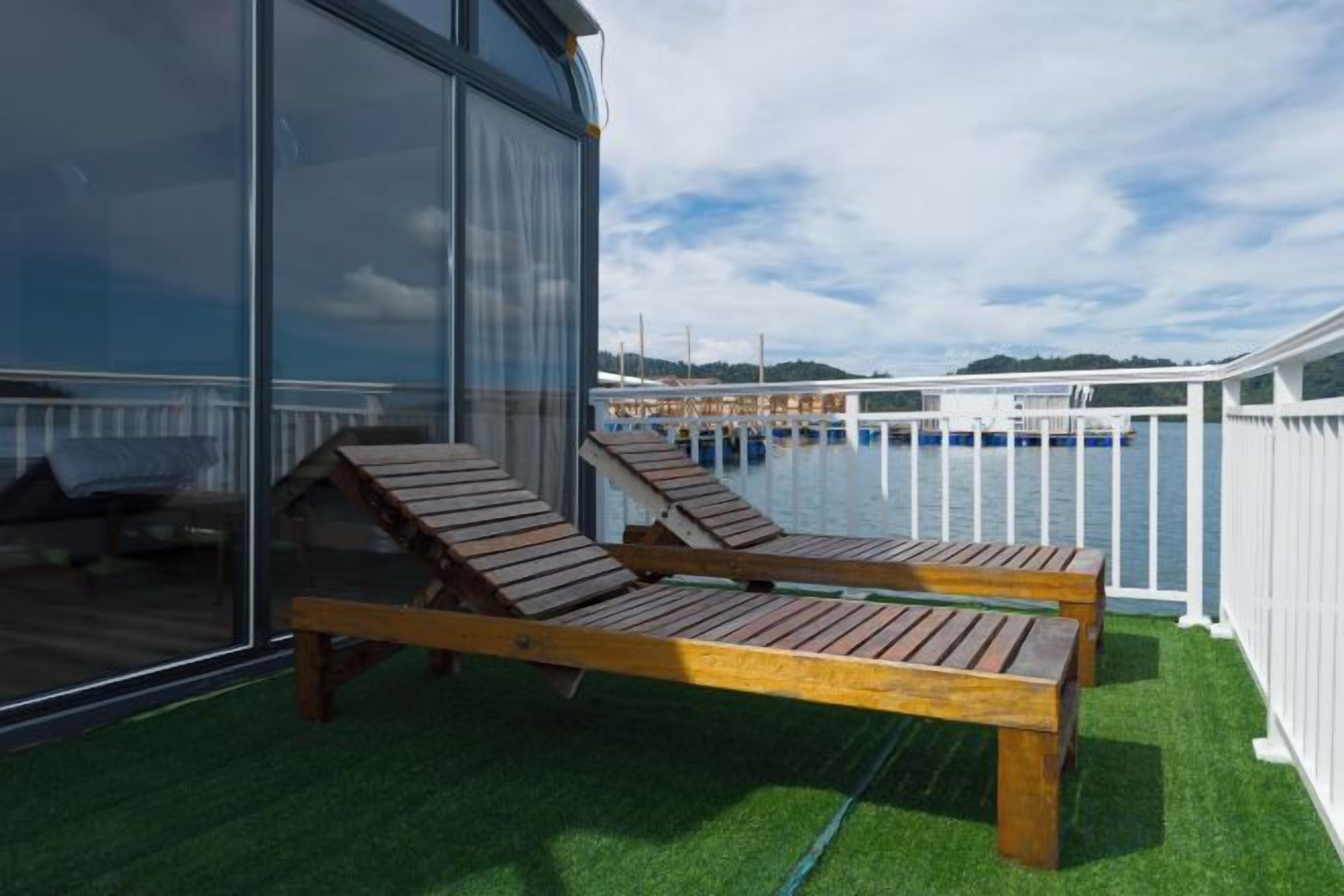 A deck with two wooden loungers, a glass wall, and a view of a marina.