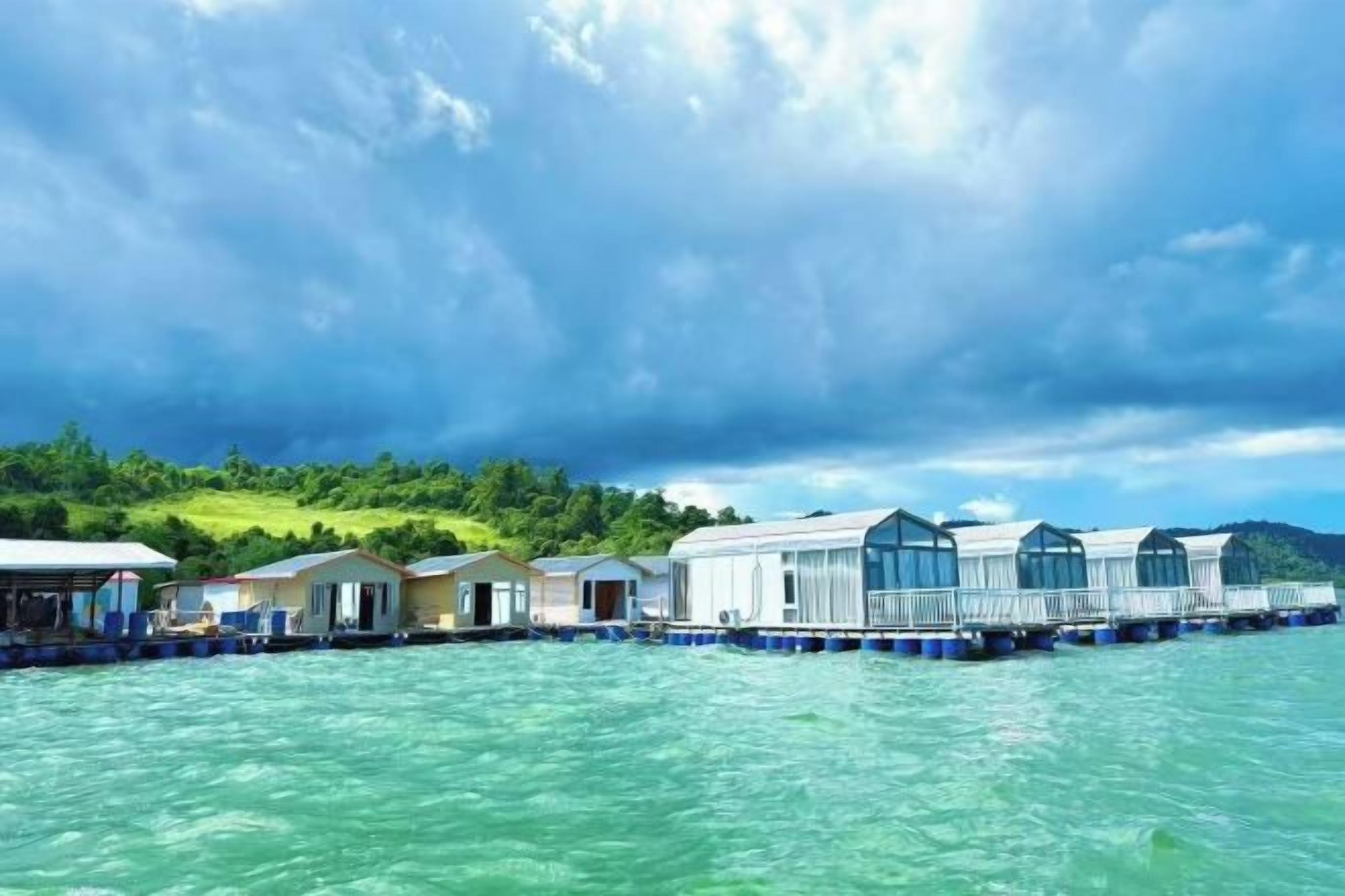 Une propriété située au bord de l’eau, dotée de bungalows sur pilotis, offrant une vue dégagée sur l’eau et s’inscrivant dans un paysage vallonné en arrière-plan.