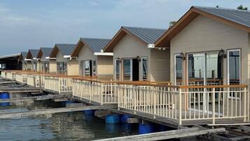 Une rangée de bungalows sur pilotis, dotés de terrasses et de rampes en bois, reliés par une passerelle flottante.