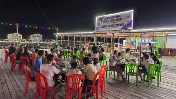 Un espace de restauration en plein air avec des tables et des chaises, une enseigne au-dessus, et une vue sur la mer.