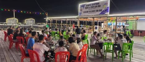 An outdoor dining area with tables and chairs, a sign overhead, and a view of the sea.