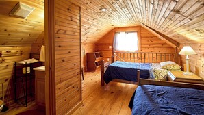 A cozy attic bedroom with a sloped ceiling, wooden walls, and a window letting in natural light.