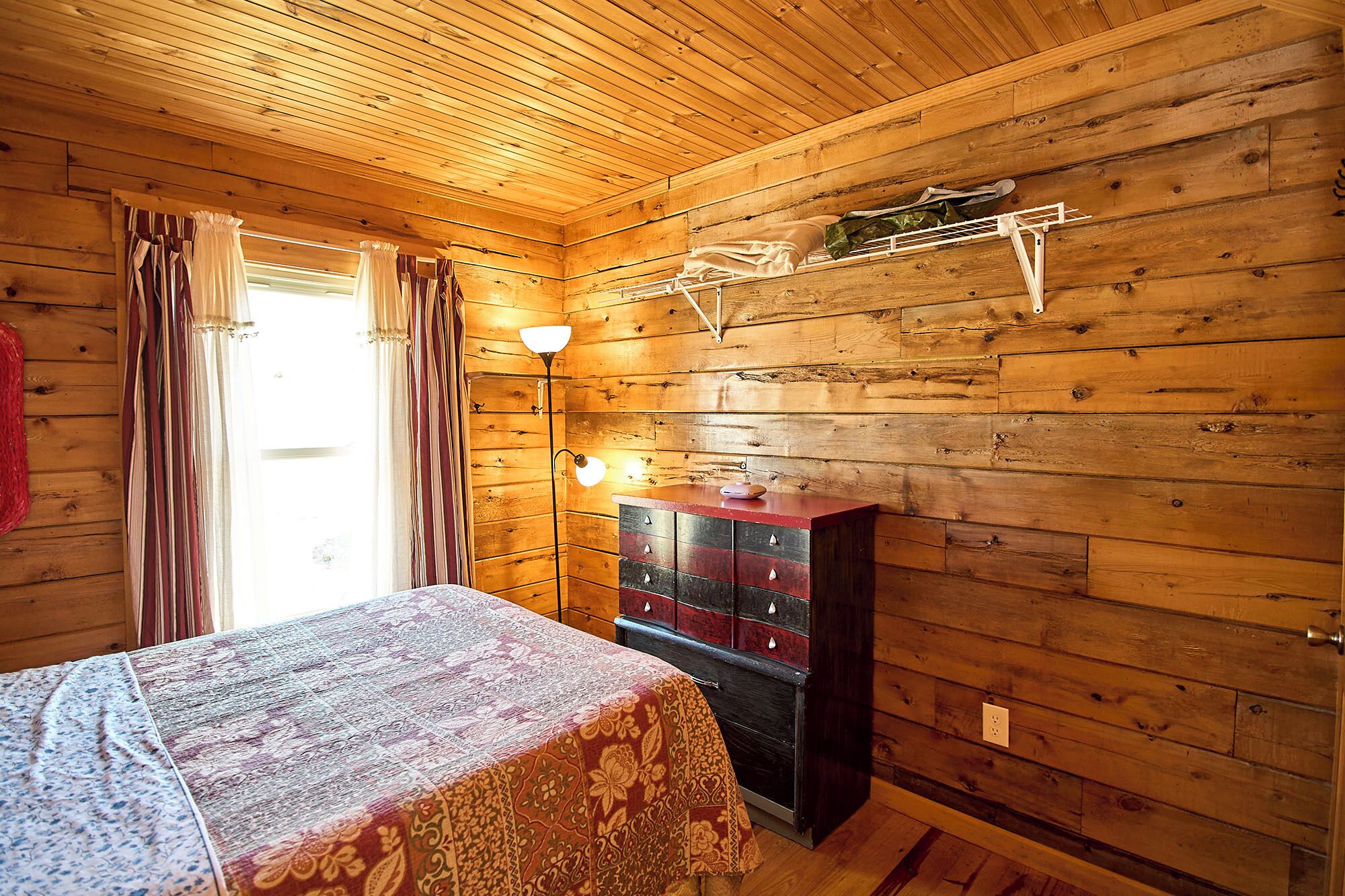 A wooden cabin room with a bed, dresser, and a hanging clothes rack.