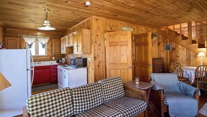 A cozy cabin interior with a kitchenette, a sofa, a chair, and a staircase.