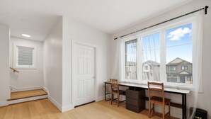 Ein Zimmer mit Schreibtisch, zwei Stühlen, einer Tür, einem Fenster mit Vorhängen, einer Treppe und einem schwarzen Lautsprecher.