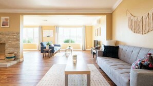 Uma sala de estar espaçosa com lareira de pedra, um sofá cinzento, uma mesa de centro e uma janela grande com cortinas.