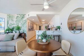 Un salon moderne avec un coin repas, comprenant un ventilateur de plafond, une grande fresque murale et une table à manger avec des chaises.