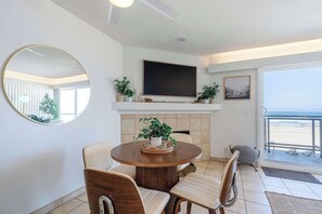 Ein Essbereich mit rundem Tisch, Stühlen, einem Kamin, einem Fernseher und Blick auf den Strand.