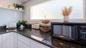 A modern kitchen with a black microwave, white cabinets, a window with a view, and decorative items on the counter.