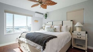 A bedroom with a large bed, a ceiling fan, a nightstand, and a window with a view.