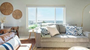 A living room with a sofa, a coffee table, and a view of the city through large windows.