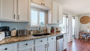 A kitchen with white cabinets, a granite countertop, a sink, and a dining area with a table and chairs.