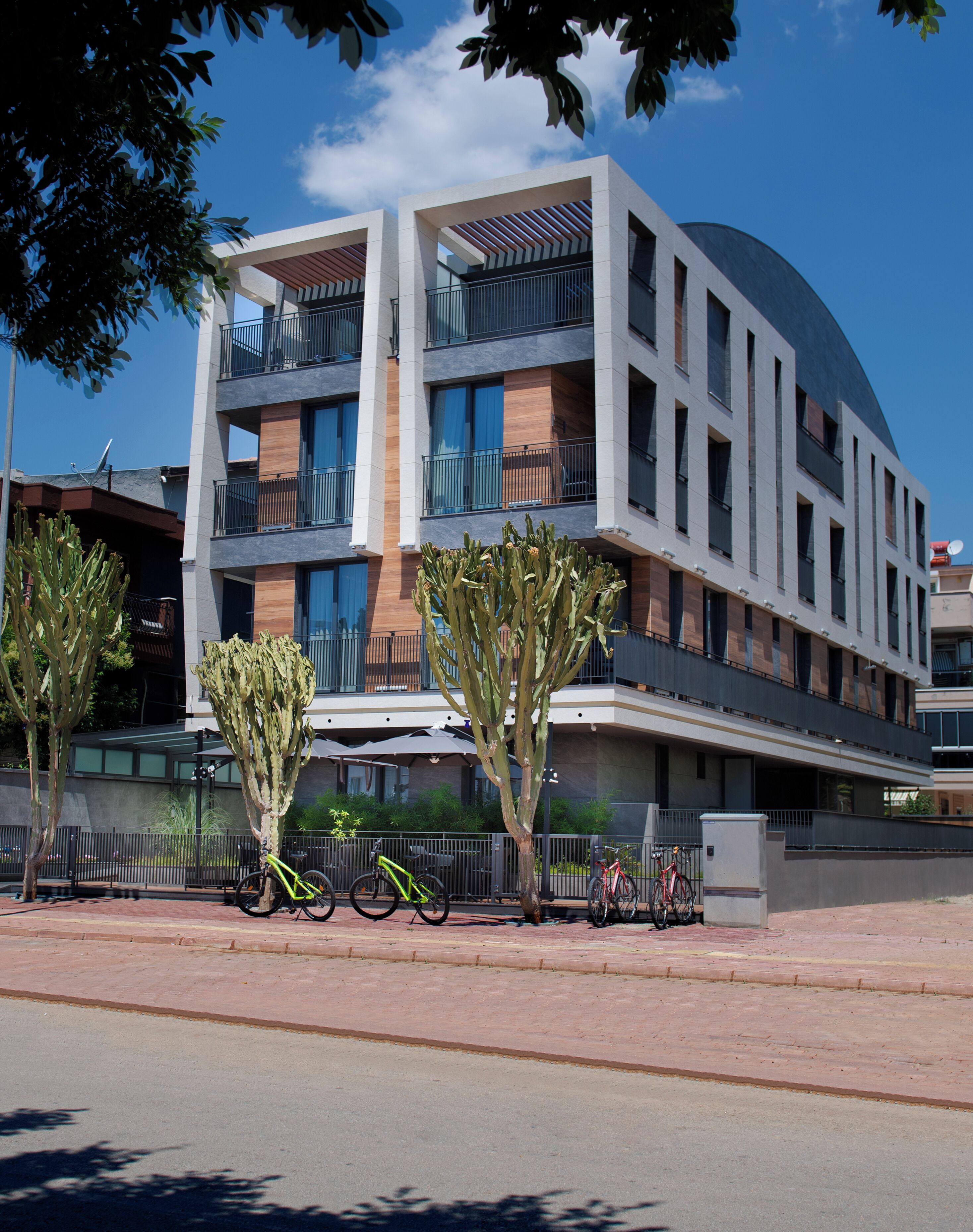 A modern multi-story building with balconies, a paved sidewalk, and bicycles parked in front.