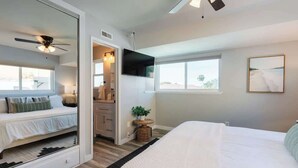 Une chambre à coucher avec un lit, une télévision, un ventilateur de plafond et une fenêtre.