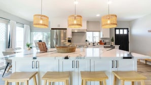 Une cuisine moderne dotée d’un îlot central, de meubles blancs et de tabourets en bois.