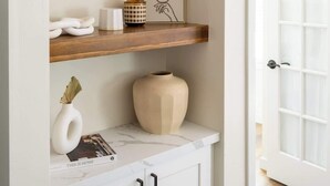 A hallway with a white door, wooden shelves with decorative items, and a marble countertop with a magazine. - Bright & Airy Mission Bay Retreat | Walk to Beach! (San Diego)