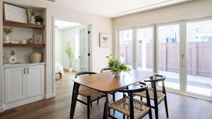 A dining area with a wooden table and woven chairs, a potted plant, and a view of a backyard through a sliding glass door. - Bright & Airy Mission Bay Retreat | Walk to Beach! (San Diego)