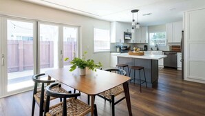 A modern kitchen with a central island, wooden flooring, and a dining area with a table and chairs. - Bright & Airy Mission Bay Retreat | Walk to Beach! (San Diego)