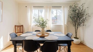 Ein Essbereich mit einem Tisch für vier Personen, umgeben von Stühlen, einer Vase mit Pflanze und einer hohen Topfpflanze seitlich.