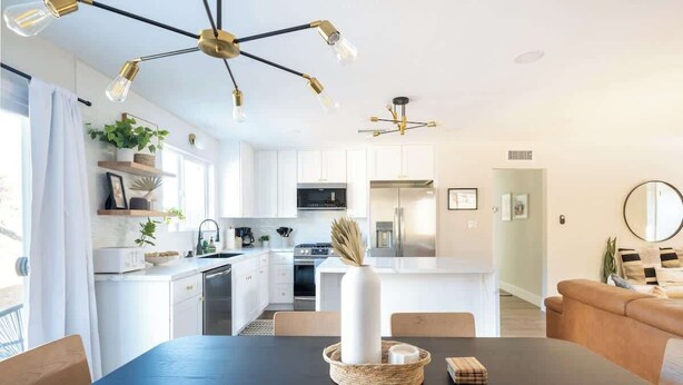 A modern kitchen with white cabinets, a central island, and a dining area with a black table.