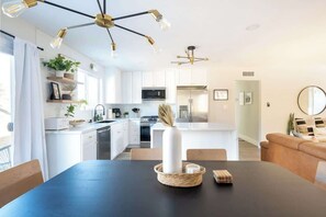 Une cuisine moderne avec des meubles blancs, un îlot central et un coin repas doté d’une table noire.