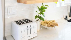 A kitchen with white cabinetry, a white countertop, a Cuisinart toaster, a framed quote, and various plants.
