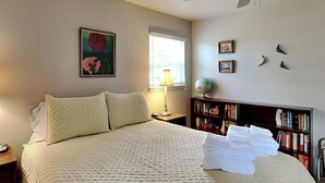 Un lit bien fait, avec une couverture matelassée, une lampe de chevet, une bibliothèque et un tableau encadré au mur.