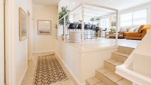 Un interior moderno con una escalera que conduce a un comedor, un sofá y una alfombra estampada.