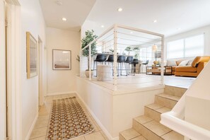 A modern interior with a staircase leading to a dining area, a sofa, and a patterned rug.