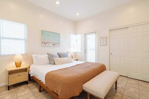 A bedroom with a bed, bedside tables, a bench, a painting, and a door.