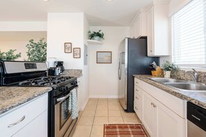 A kitchen with a stove, oven, refrigerator, and sink. There are cabinets, a countertop, and a rug.
